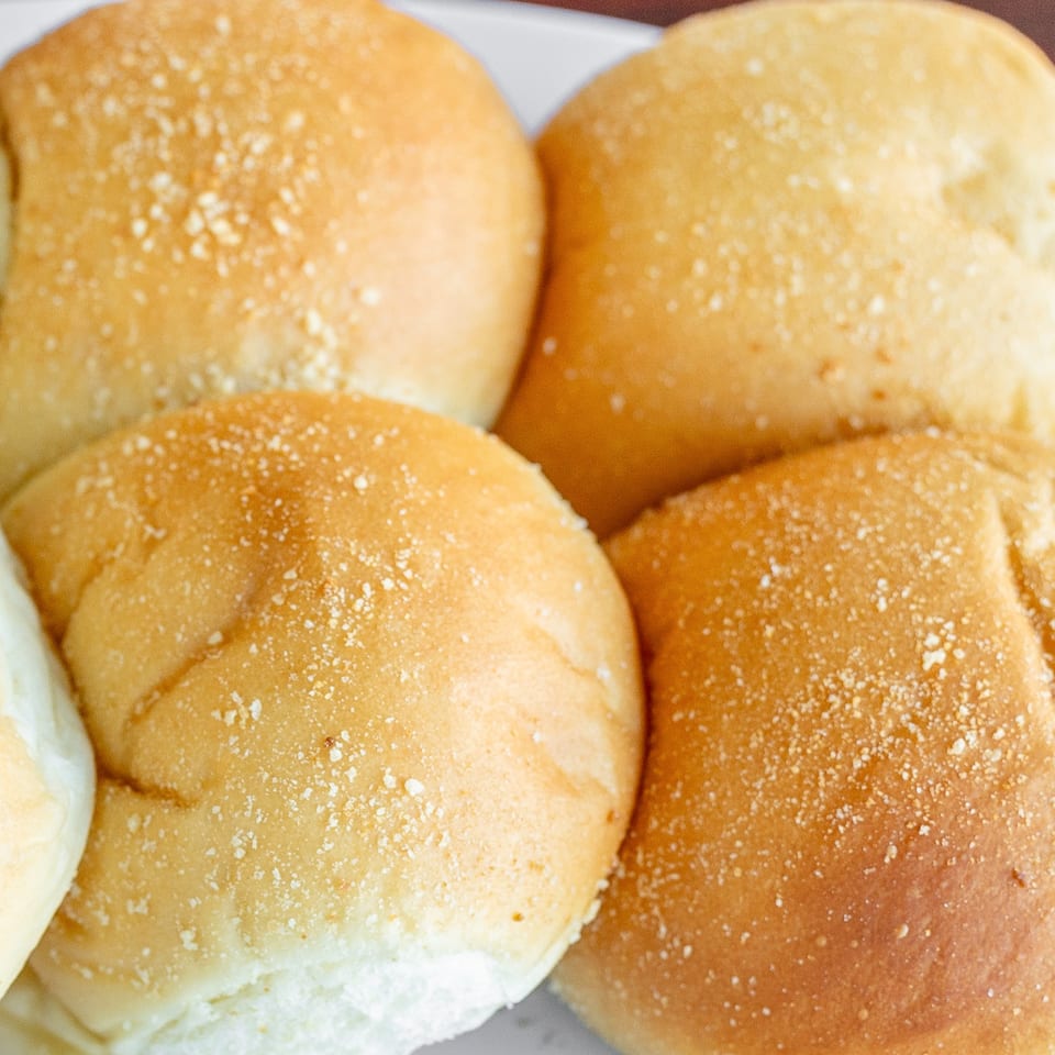Close-up of several golden-brown Filipino pandesal rolls, lightly dusted with breadcrumbs.