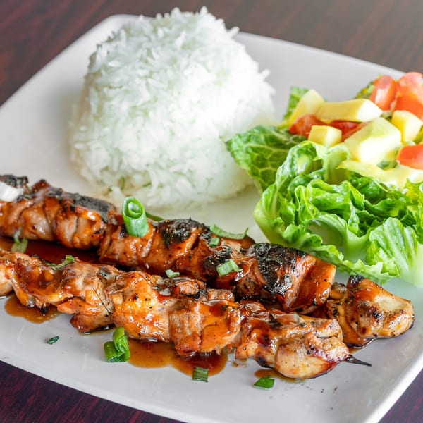 Filipino chicken skewers with a sweet glaze, white rice, and a fresh salad on a white plate.