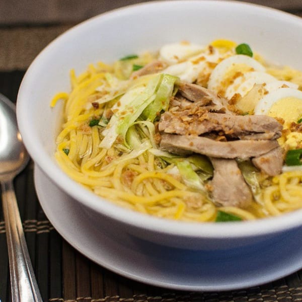 Filipino pancit molo soup with noodles, sliced meat, cabbage, and hard-boiled eggs in a white bowl.