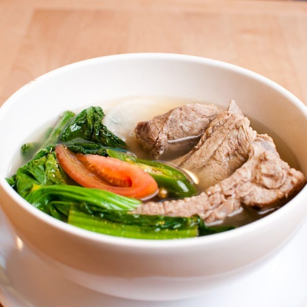Filipino Sinigang soup with pork ribs, green vegetables, tomato, and chili in a white bowl.