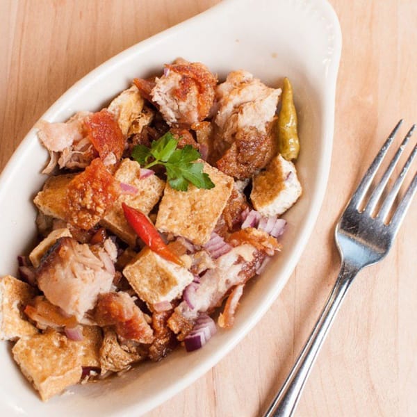 Filipino sisig with crispy pork, tofu, red onions, and chili peppers in a white dish with a fork.